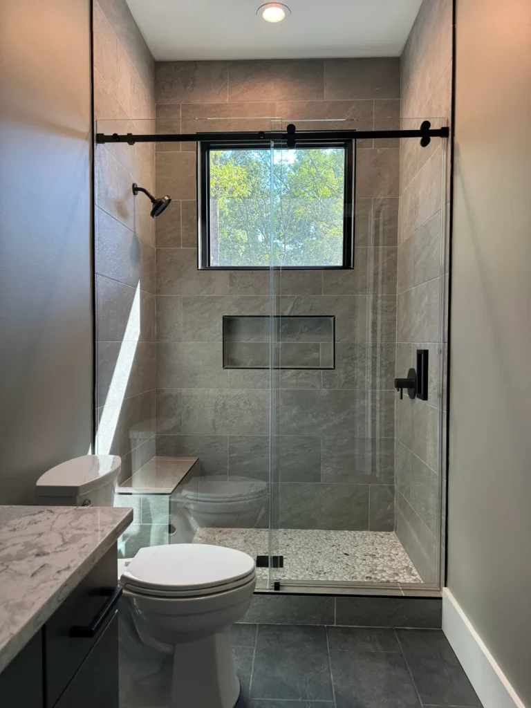 Gray tile walk-in shower with window and black-framed sliding glass door