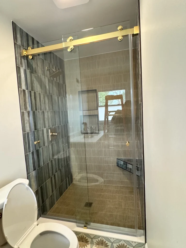 Green vertical tile shower with gold sliding glass door