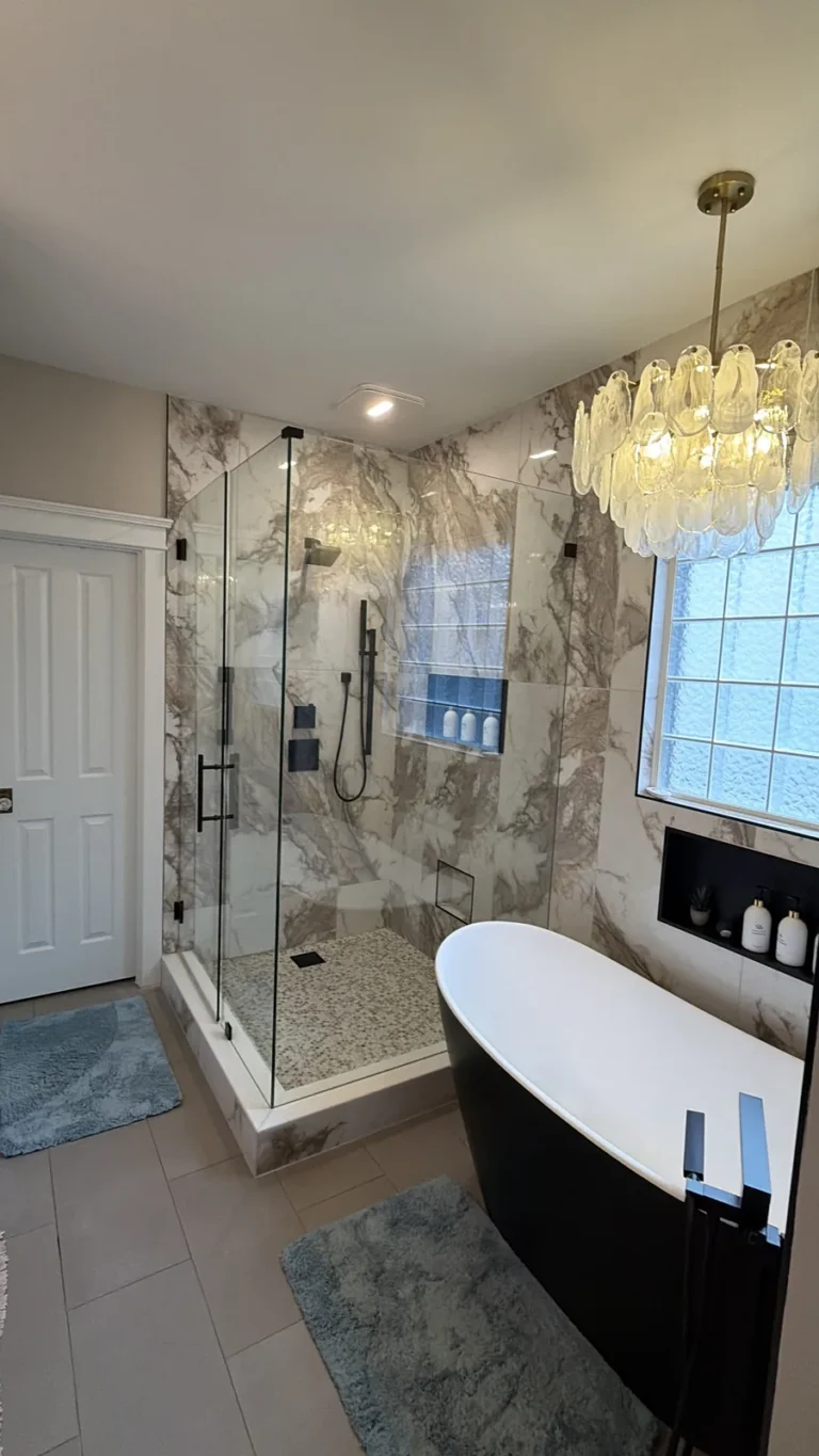 Marble-look tile shower with black freestanding tub and chandelier