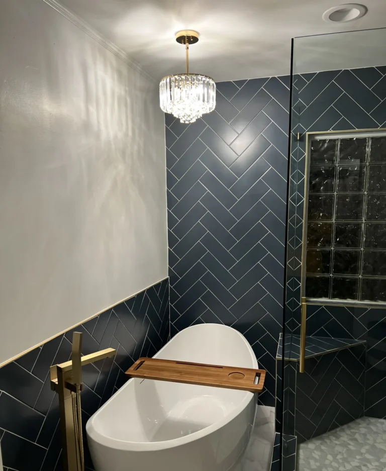 Freestanding tub with gold floor-mounted faucet, crystal chandelier and navy herringbone tile, Charlotte area