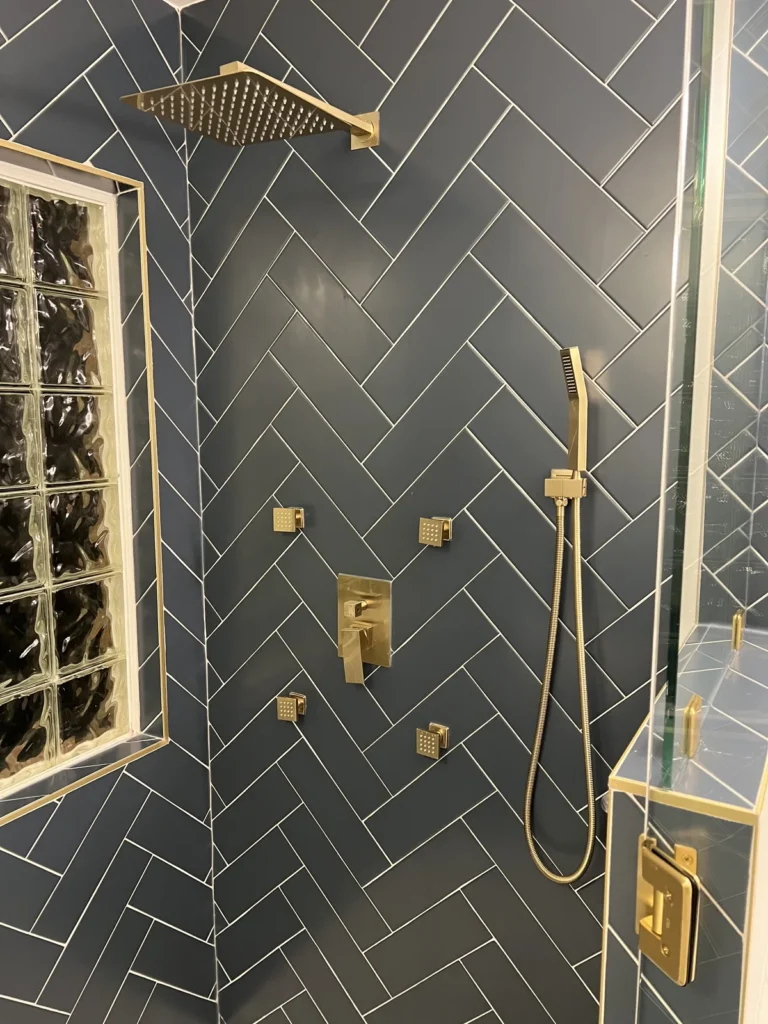Gold rain shower head, body sprays and handheld shower on navy herringbone tile, Charlotte area