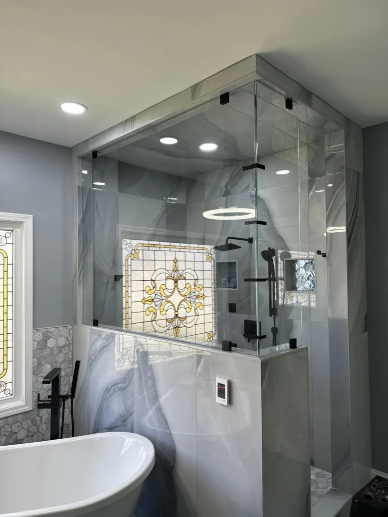 Floor-to-ceiling glass steam shower enclosure with marble-look tile and freestanding tub