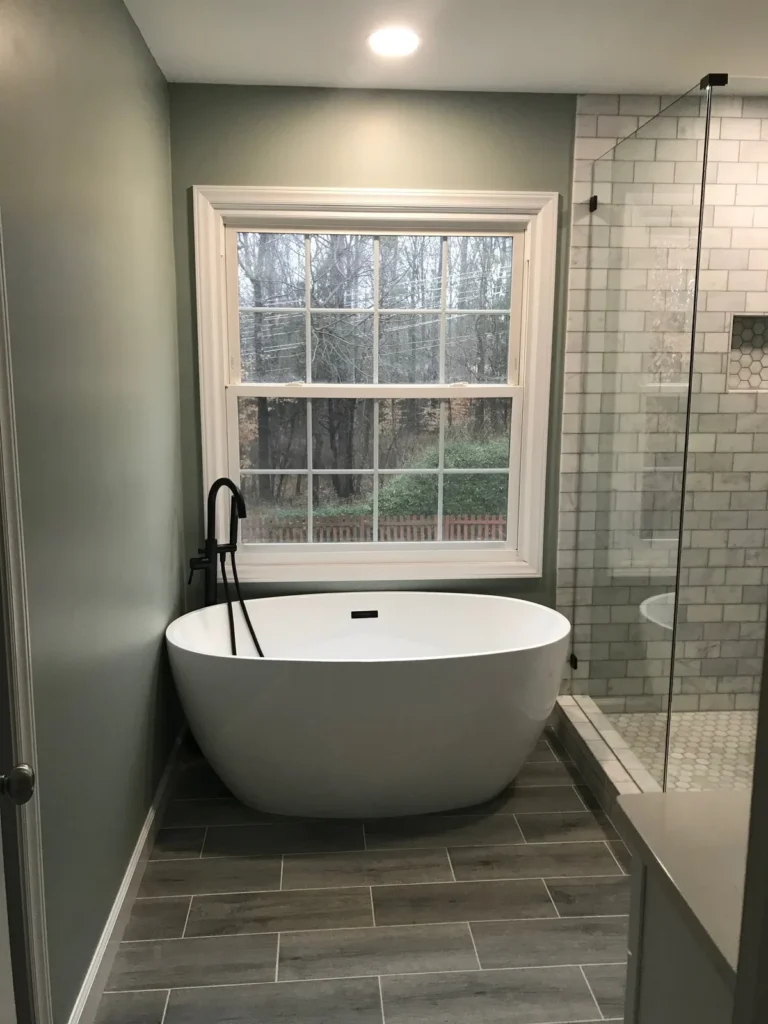 White freestanding tub under a window beside a white subway tile shower